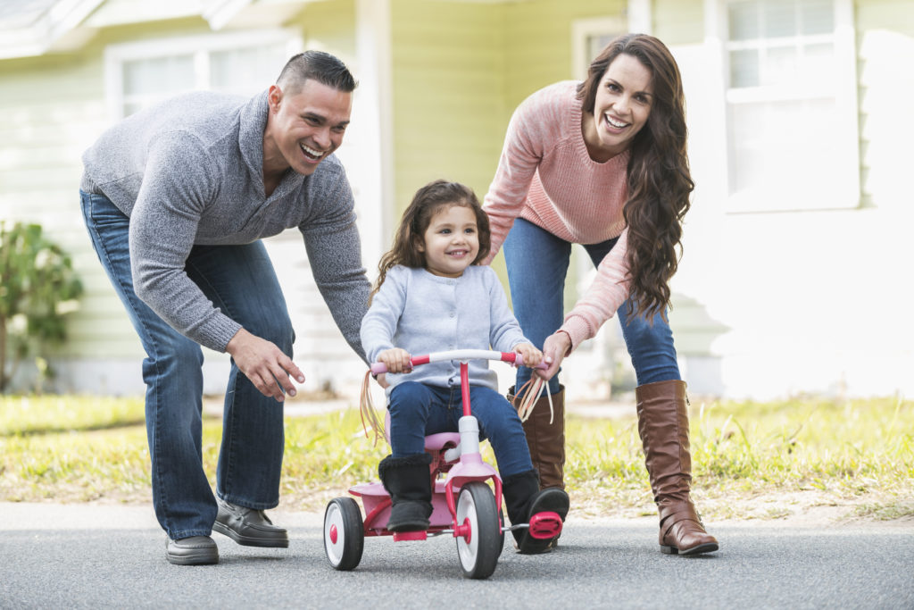 Hispanic parents helping girl ride tricycle