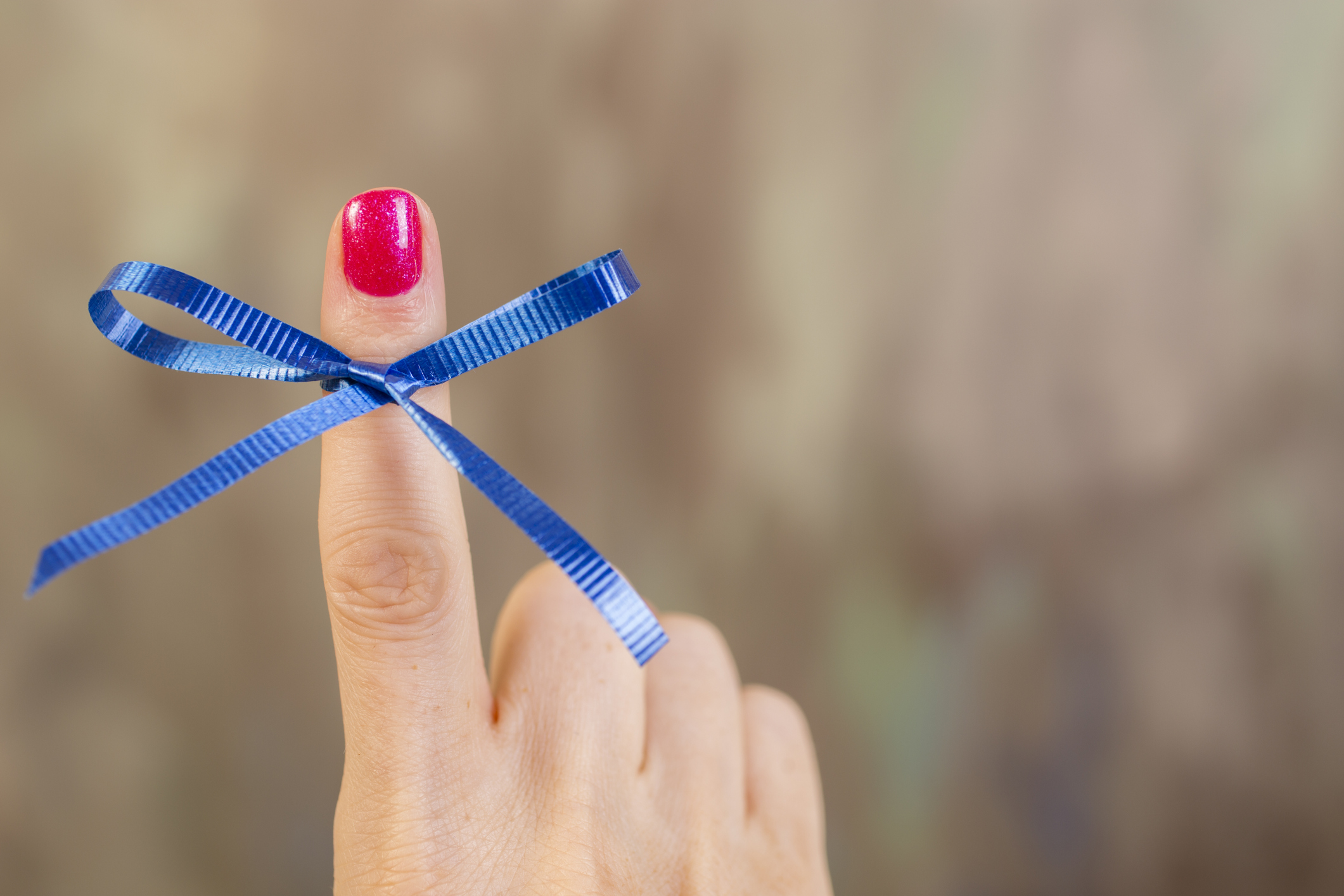 Blue social awareness ribbon tied in a bow around a woman's index finger. The blue ribbon represents various causes including: drunk driving, child abuse prevention, water quality/safety, arthritis, education, anti-tobacco, and colon cancer. Gray background. Copyspace.